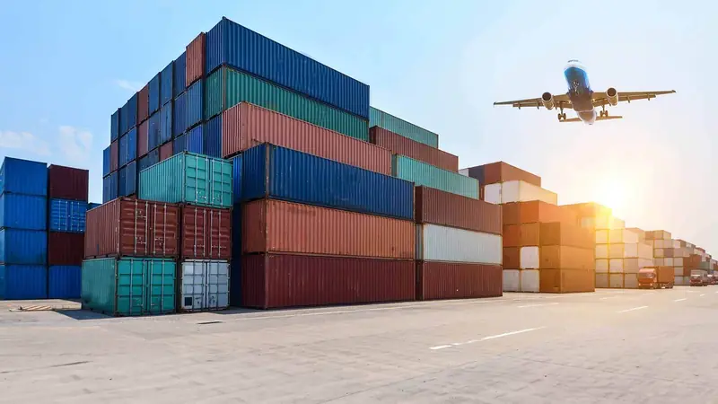 Container yard at low sun with an aircraft climbing out overhead